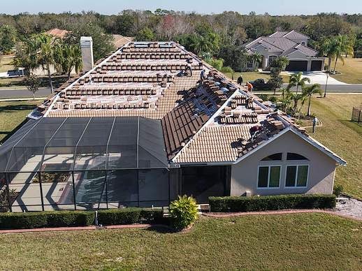 Aerial view of a residential home with solar panels on the roof and a screened pool area surrounded by landscaping and trees